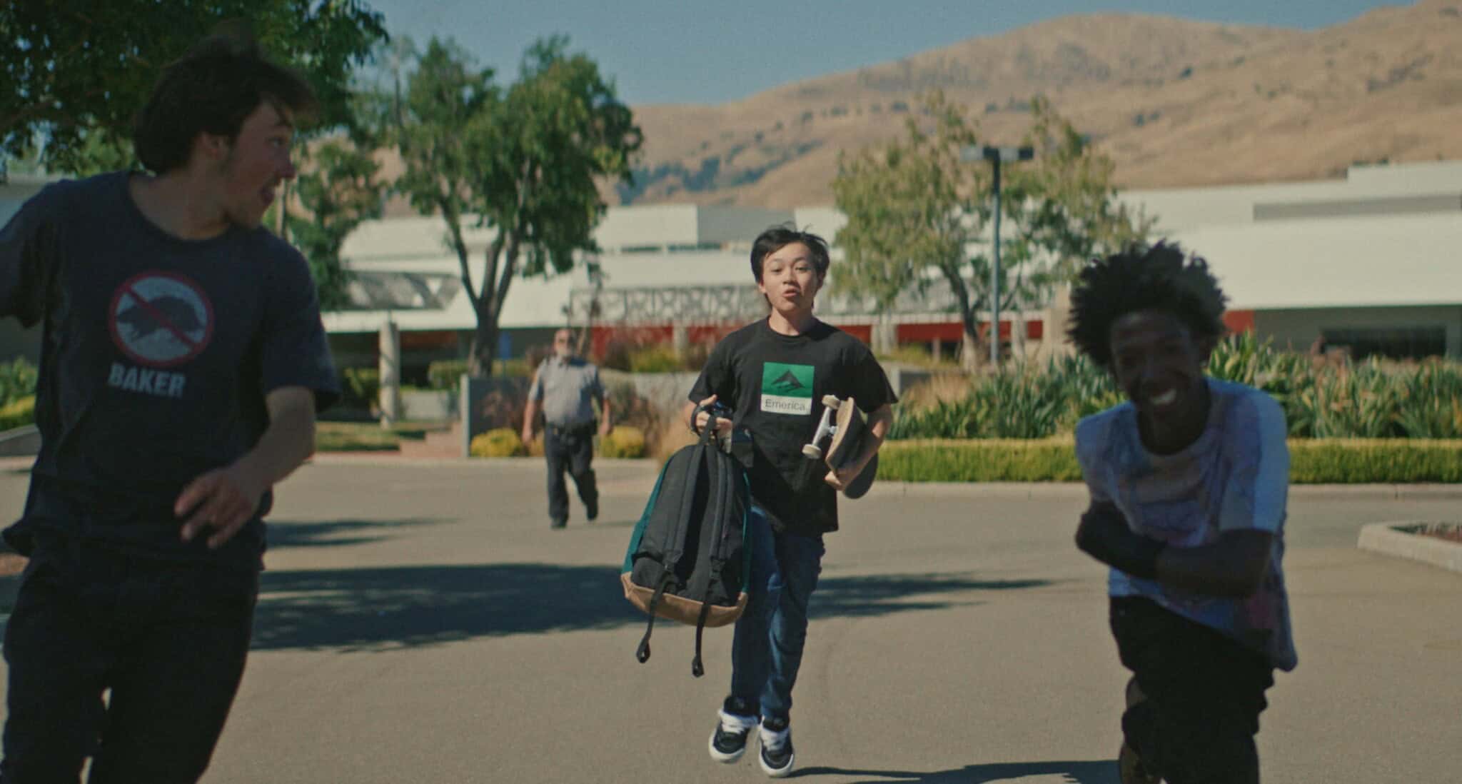 Three teenaged boys run and skate away from a security officer in "Didi."