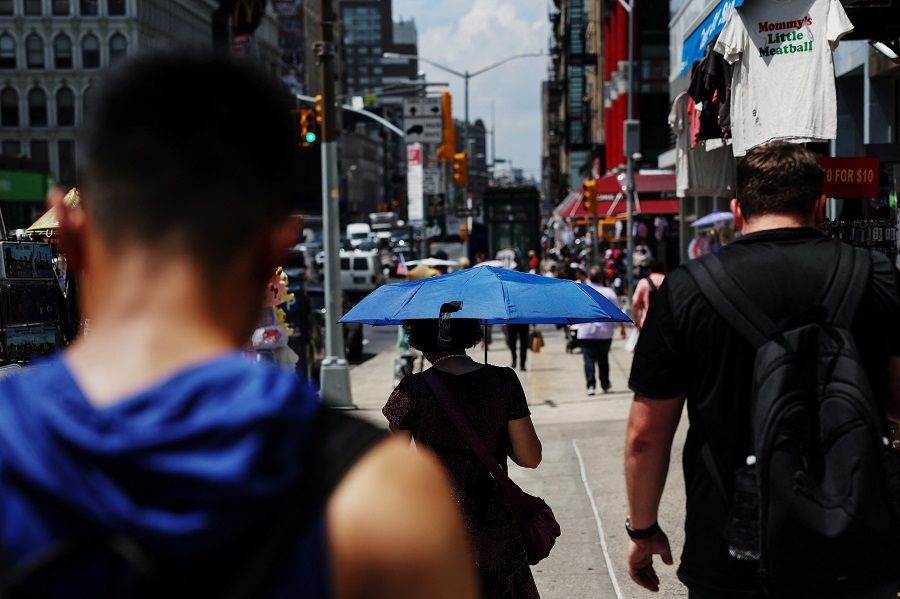 A woman walks with a parasol with others along Canal Street in the Chinatown area of New York City, US on 10 July 2024.  (Shannon Stapleton/Reuters)