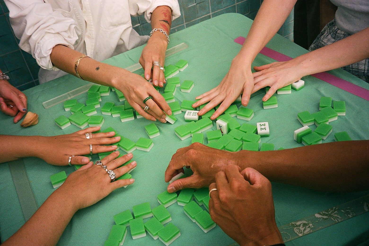 Hands reach out to flip over mahjong tiles on a green table.