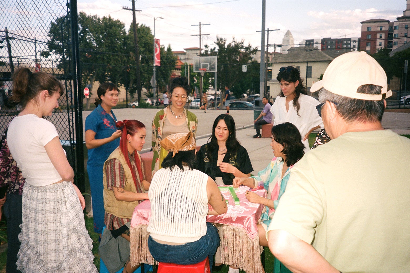 People gather around a table with mahjong played on it beside a basketball court.