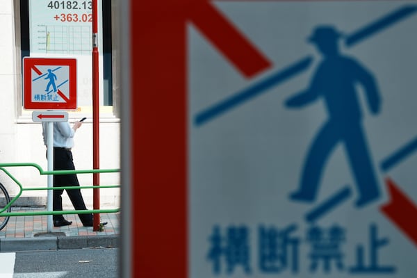A person stands near an electronic stock board, left top, showing Japan's Nikkei index at a securities firm Tuesday, July 22, 2025, in Tokyo. The traffic signs read: No Crossing. (AP Photo/Eugene Hoshiko)