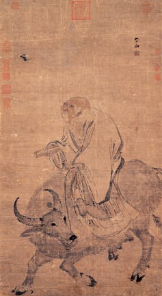 A faded scroll with a bit of Chinese script shows an elderly man in a robe sitting on top of an ox.