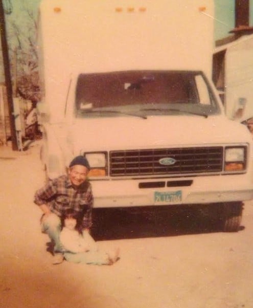 A young Ellen Kamei sits next to her grandfather Kenzo Kamei in front of a truck in a black and white family photo