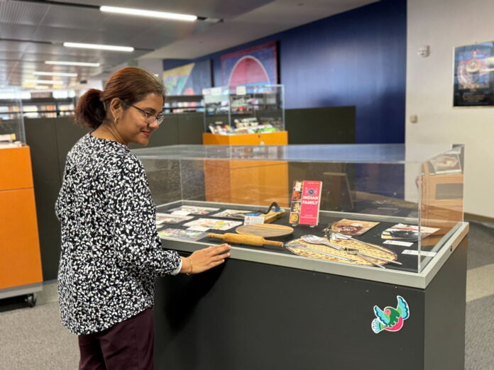 SJSU Librarian Mantra Roy checks on one of the exhibit cases that displays cooking utensils used across South Asia. Photo: Lesley Seacrist.